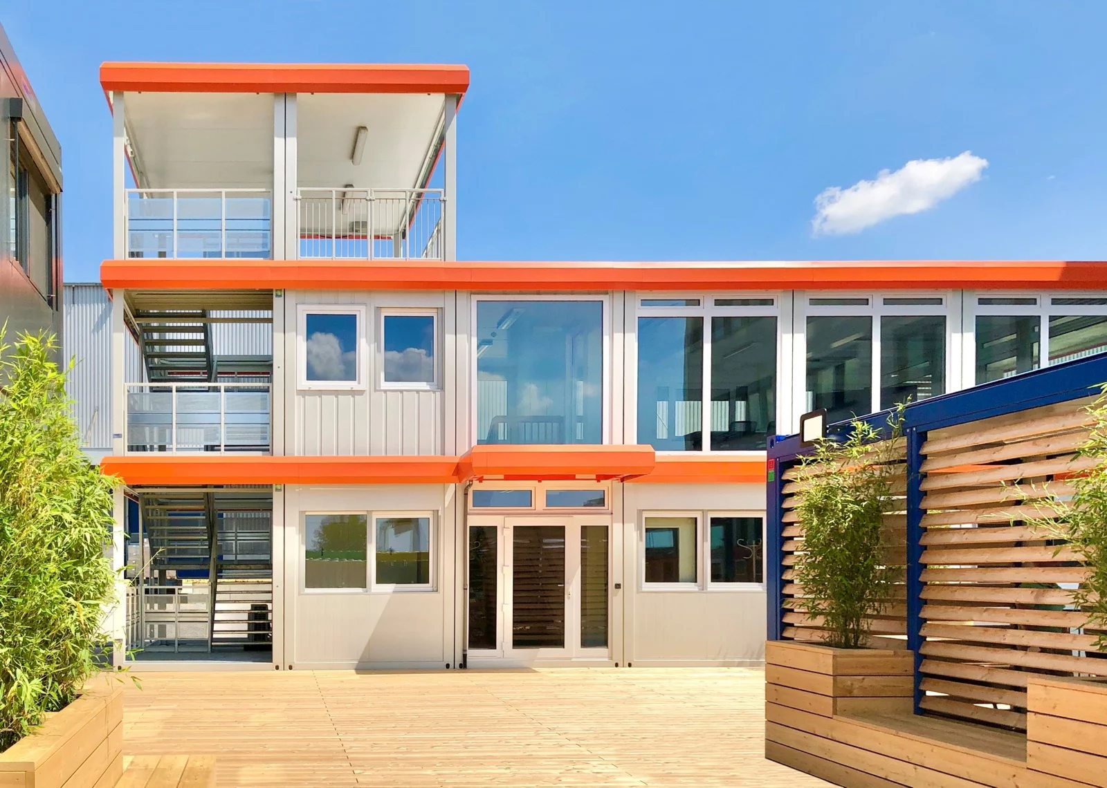 Dreigeschossige Containeranlage mit orangefarbener Attika und Vordächern
