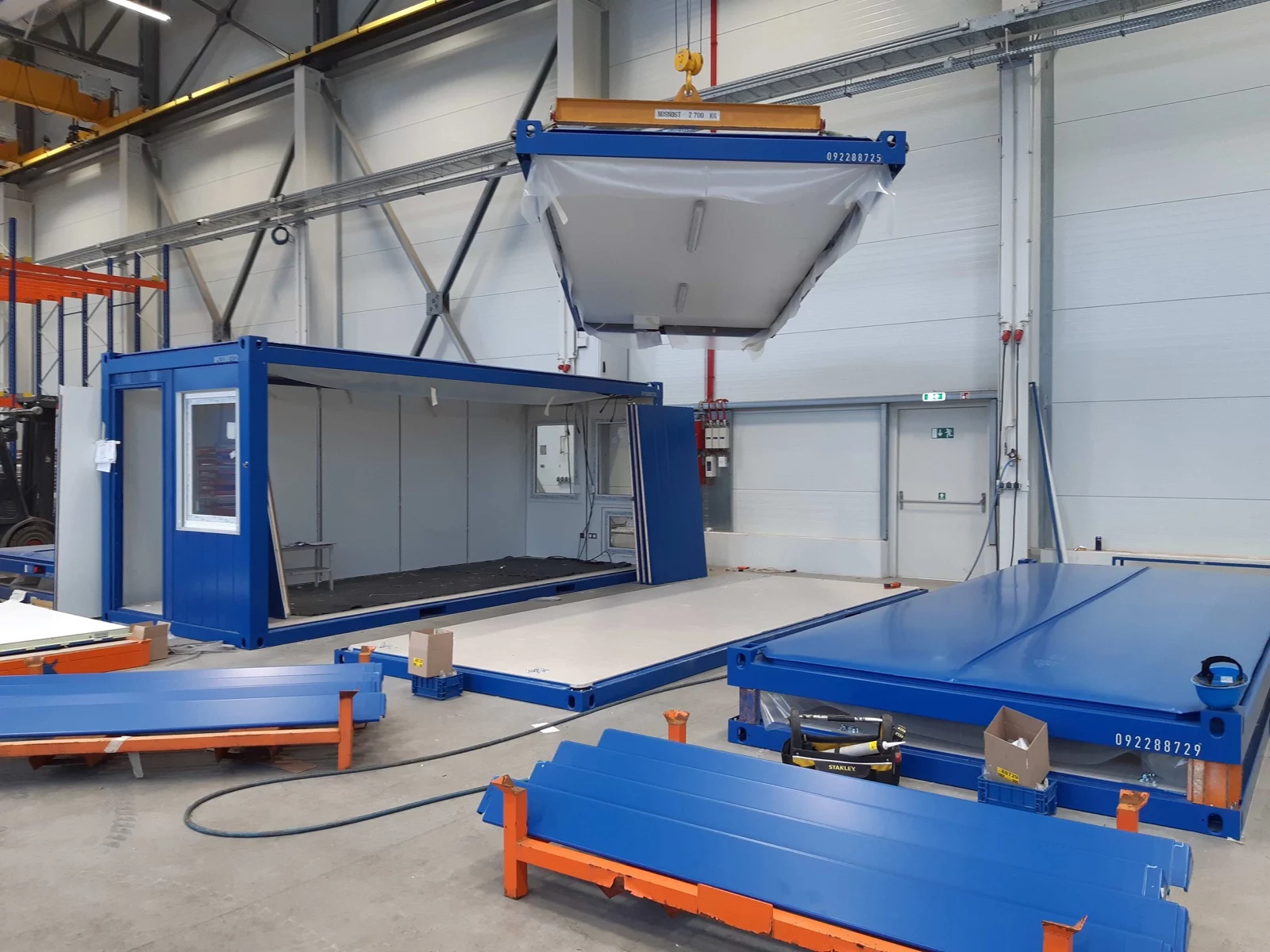 Blauer Container im Ausbau in einer Werkhalle, darüber ein Dachrahmen am Kran