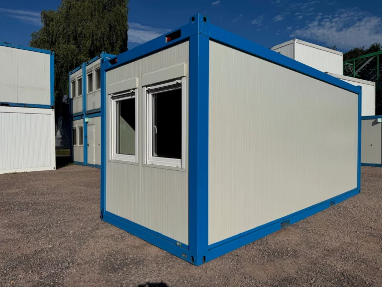 20-Fuß-Bürocontainer RAU-020 in Grauweiß mit enzianblauem Rahmen, Stirnseite mit zwei Fenstern und Längsseite, im Depot Sittensen