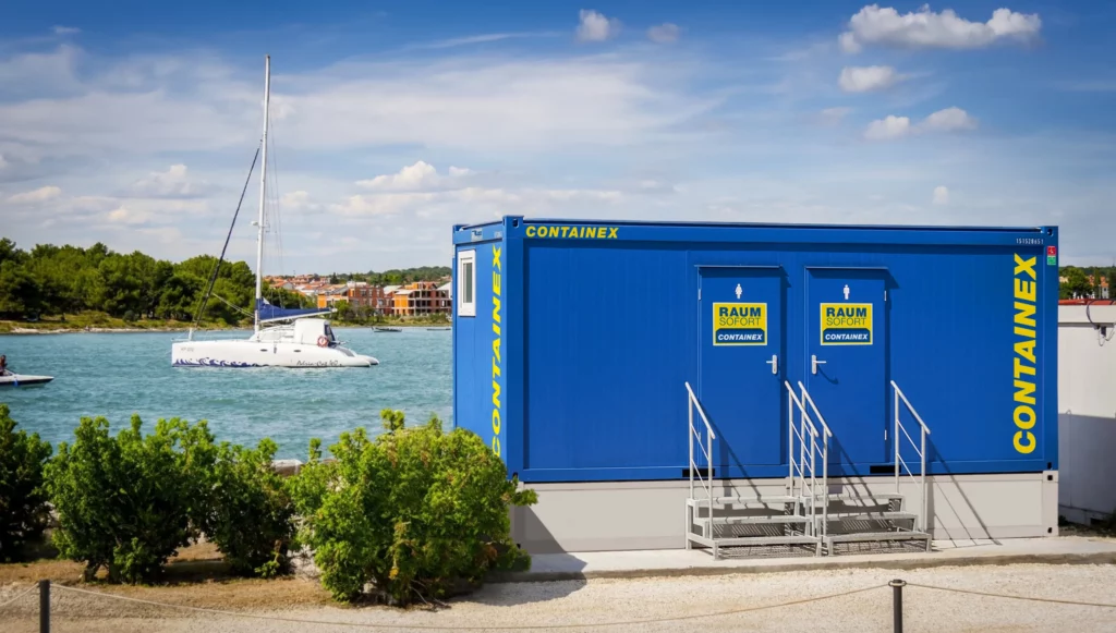Blauer WC-Container der CLASSIC Line mit zwei Eingängen und Treppen an einem Hafen