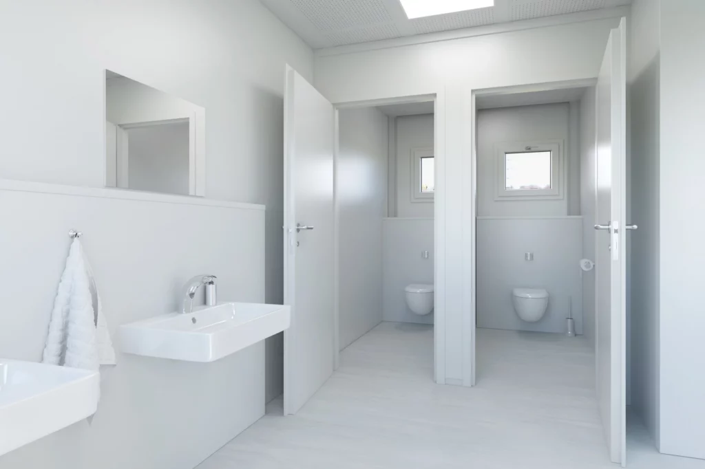 Waschraum der PLUS Line mit Keramikwaschbecken, WC-Kabinen und Leitungen unter Putz