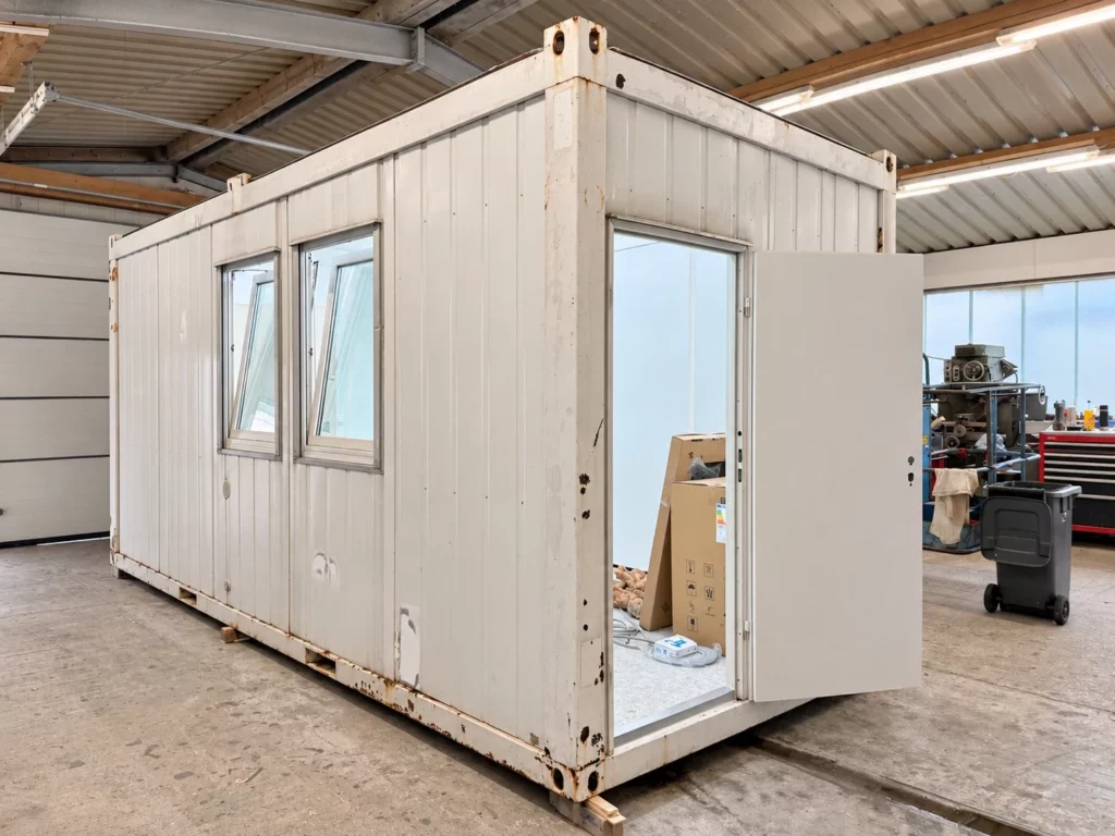 Gebrauchter Container in der Werkstatt mit neu gesetzten Fenstern und offener neuer Außentür