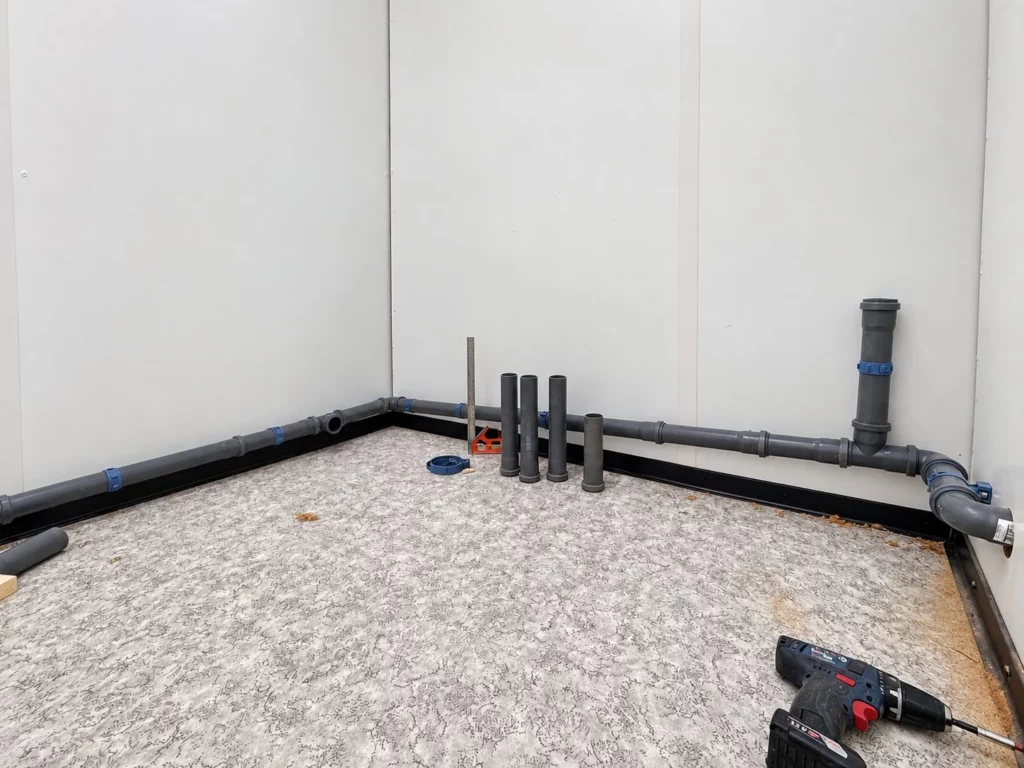 Abwasserleitungen aus grauem Kunststoffrohr an der Wand des Sanitärraums vor dem Einbau von WC und Waschbecken