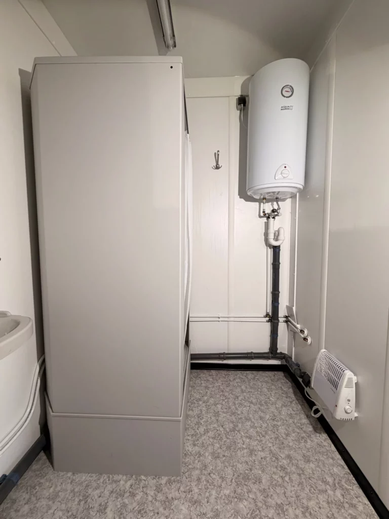 Fertiges Bad mit Duschkabine, Warmwasserspeicher an der Wand und Heizlüfter