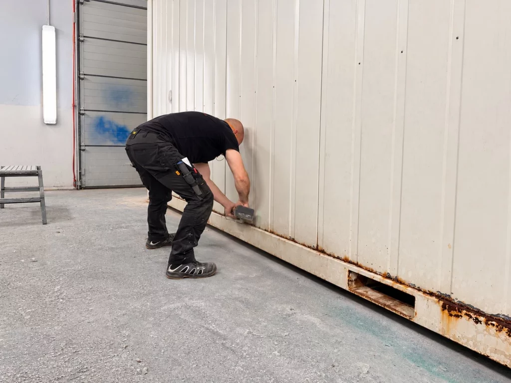 Mitarbeiter schleift den rostigen Bodenrahmen eines Containers in der Werkstatt
