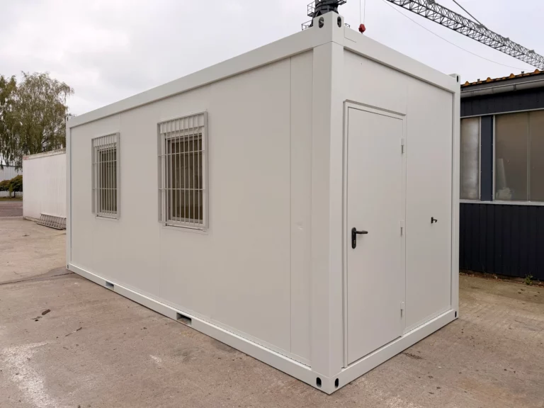 Bürocontainer 20 ft in Lichtgrau mit Eingangstür an der Stirnseite und zwei vergitterten Fenstern an der Längsseite.